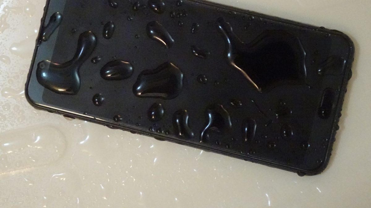 Celular preto coberto de gotas de água, deitado numa pia clara