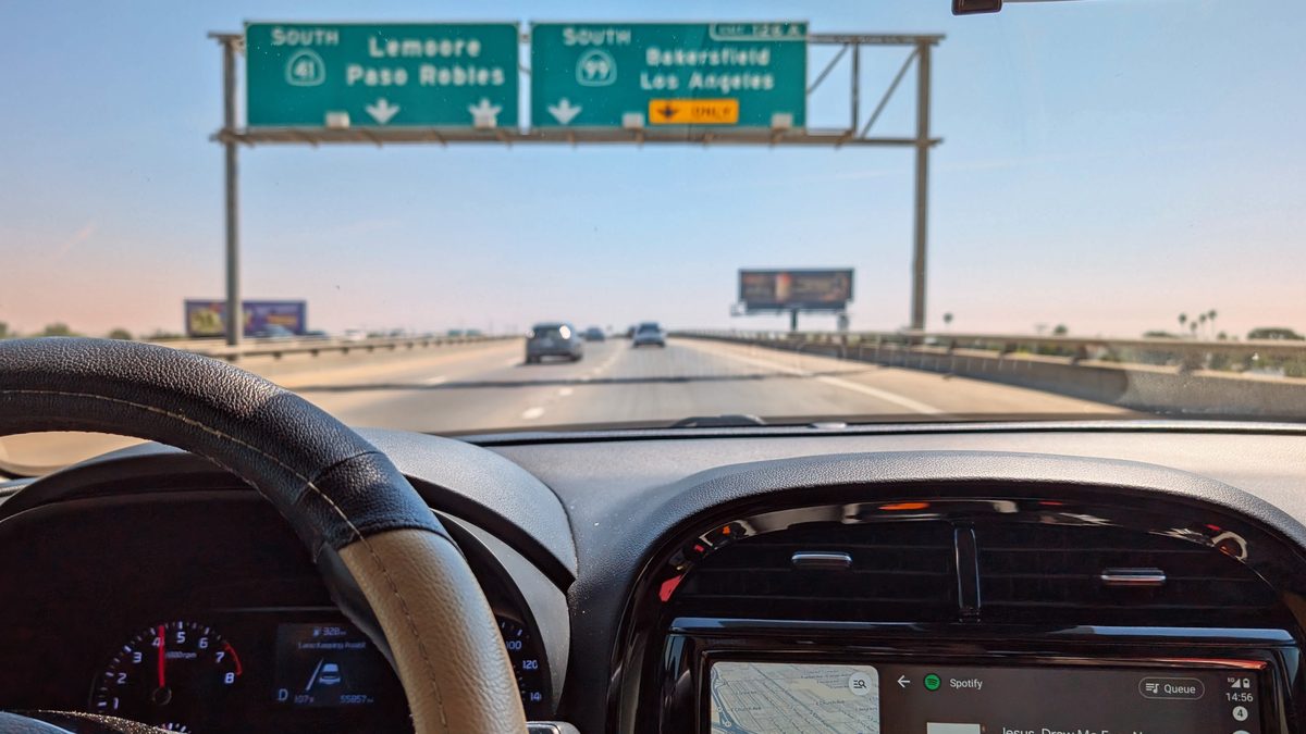 Visão do banco do motorista de um carro numa rodovia, com a tela central mostrando o Android Auto com mapa e player de música