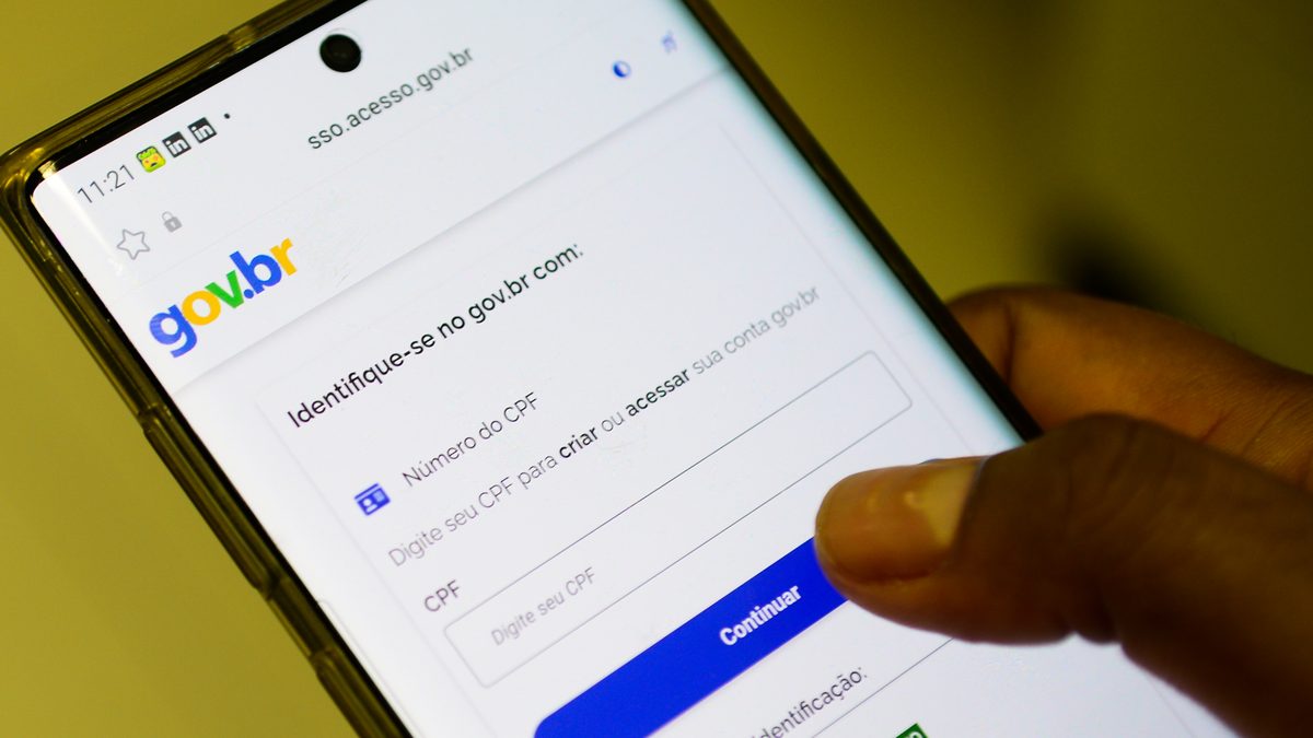 Mão segura celular com a tela de identificação do gov.br, com o campo para digitar o CPF e o botão Continuar
