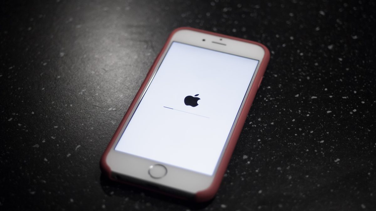 iPhone de capa rosa sobre uma mesa escura, com a tela branca mostrando o logotipo da Apple e a barra de progresso da atualização