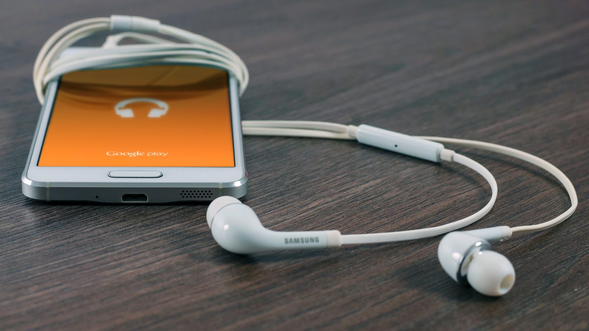 Celular sobre uma mesa de madeira com a tela laranja do Google Play Música e fones de ouvido brancos enrolados