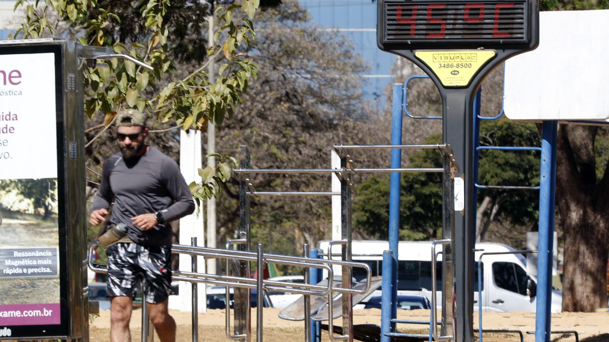 Homem corre no Parque da Cidade, em Brasília, ao lado de um termômetro de rua que marca 45 °C