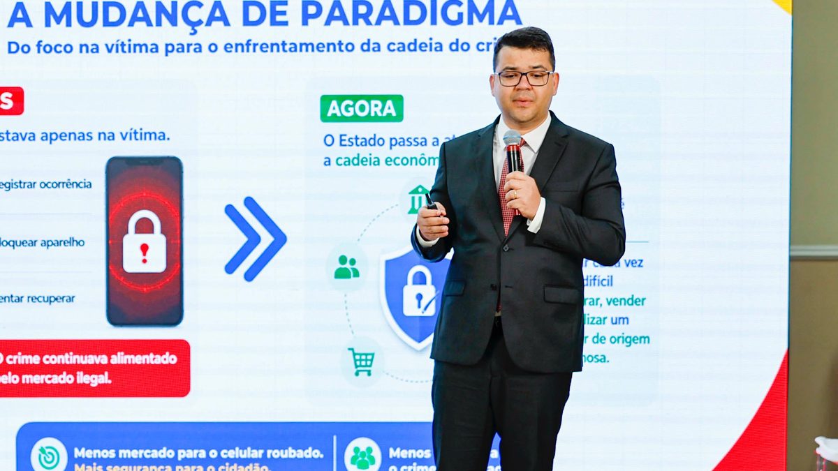 Apresentação do Programa Celular Seguro na Base Aérea de São Paulo, em 23/06/2026: expositor de terno ao lado de slide que compara o foco antes e agora no combate ao roubo de celular