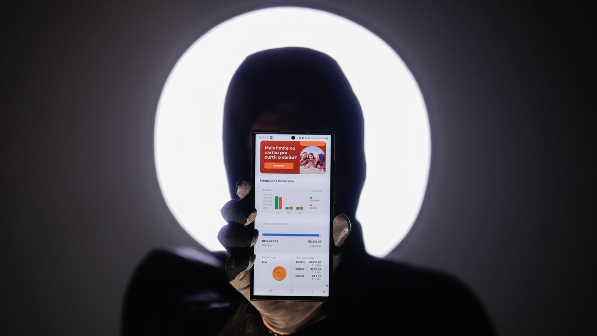 Pessoa de capuz esconde o rosto atrás de um celular