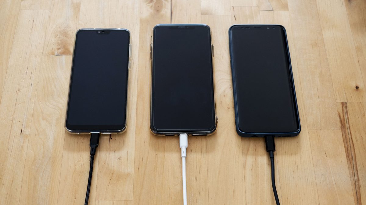Três celulares carregando sobre uma mesa de madeira clara