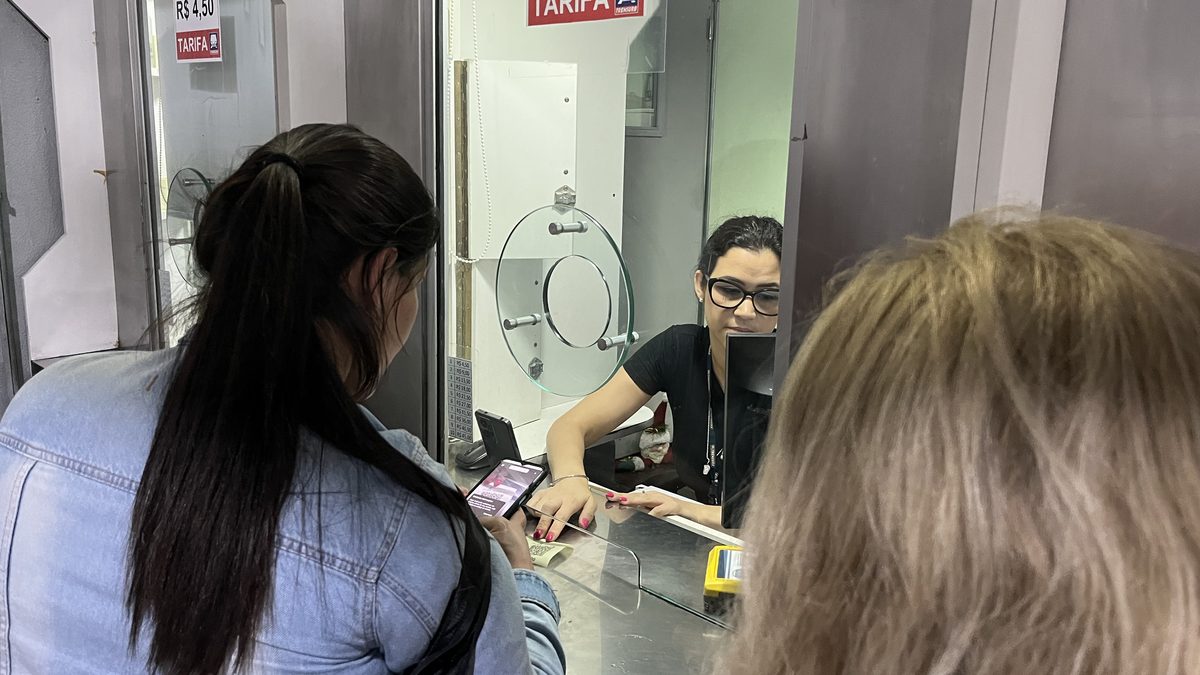 Cliente com o celular aberto no Pix diante da atendente, no guichê de pagamento