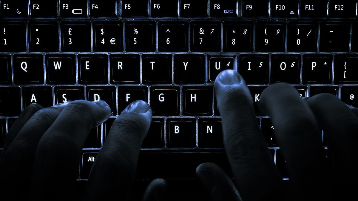 Mãos digitando no escuro em um teclado de notebook com as teclas iluminadas