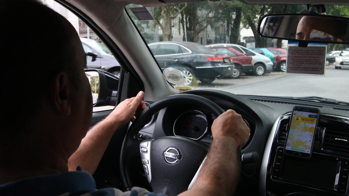Motorista de aplicativo dirige em São Paulo com o celular preso ao painel e o app aberto, visto do banco de trás