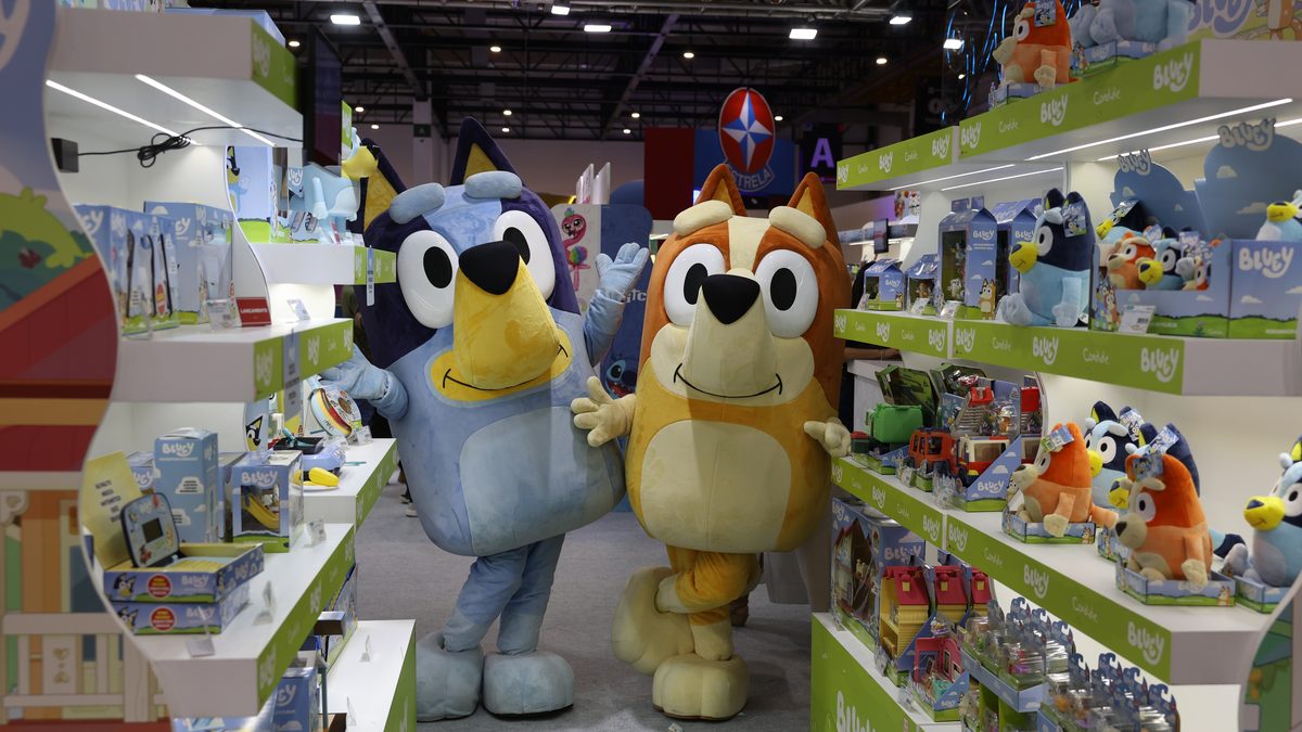 Personagens Bluey e Bingo fantasiados entre prateleiras cheias de brinquedos, em estande de uma feira do setor