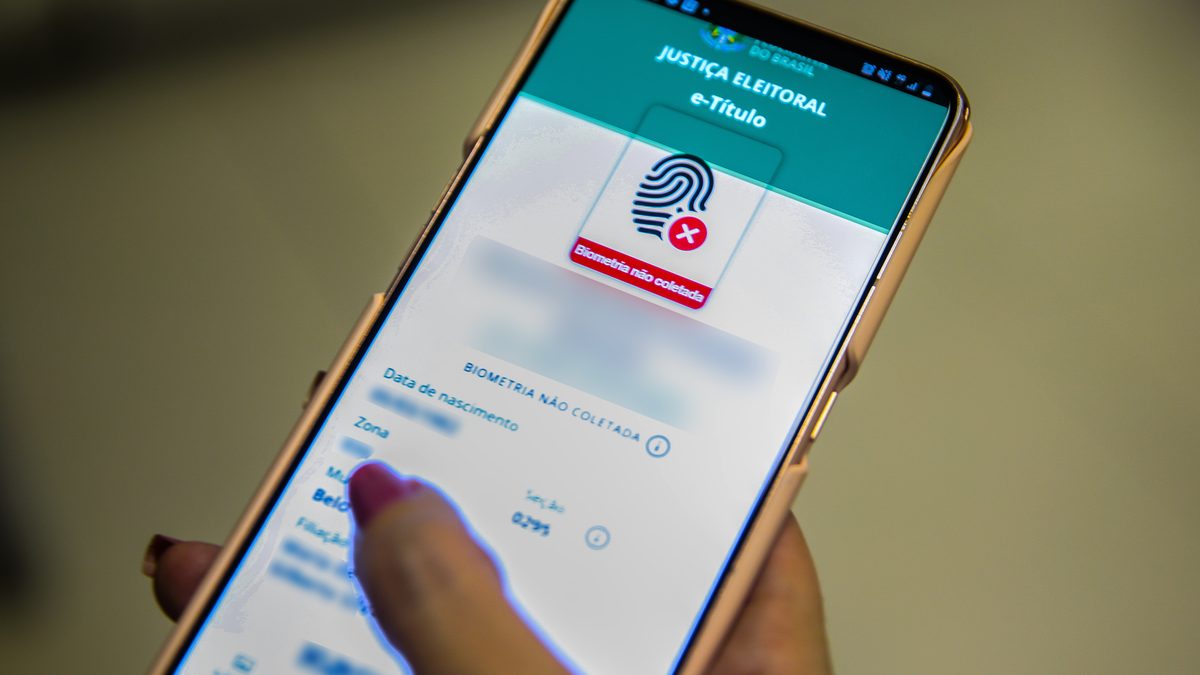 Mão segura um celular com a tela do aplicativo e-Título, da Justiça Eleitoral, com o aviso de biometria não coletada
