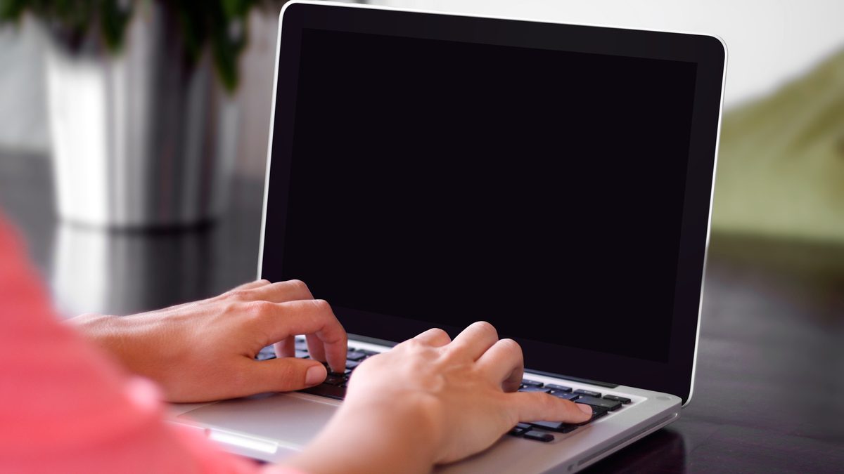 Mãos digitando em um notebook aberto sobre uma mesa de madeira