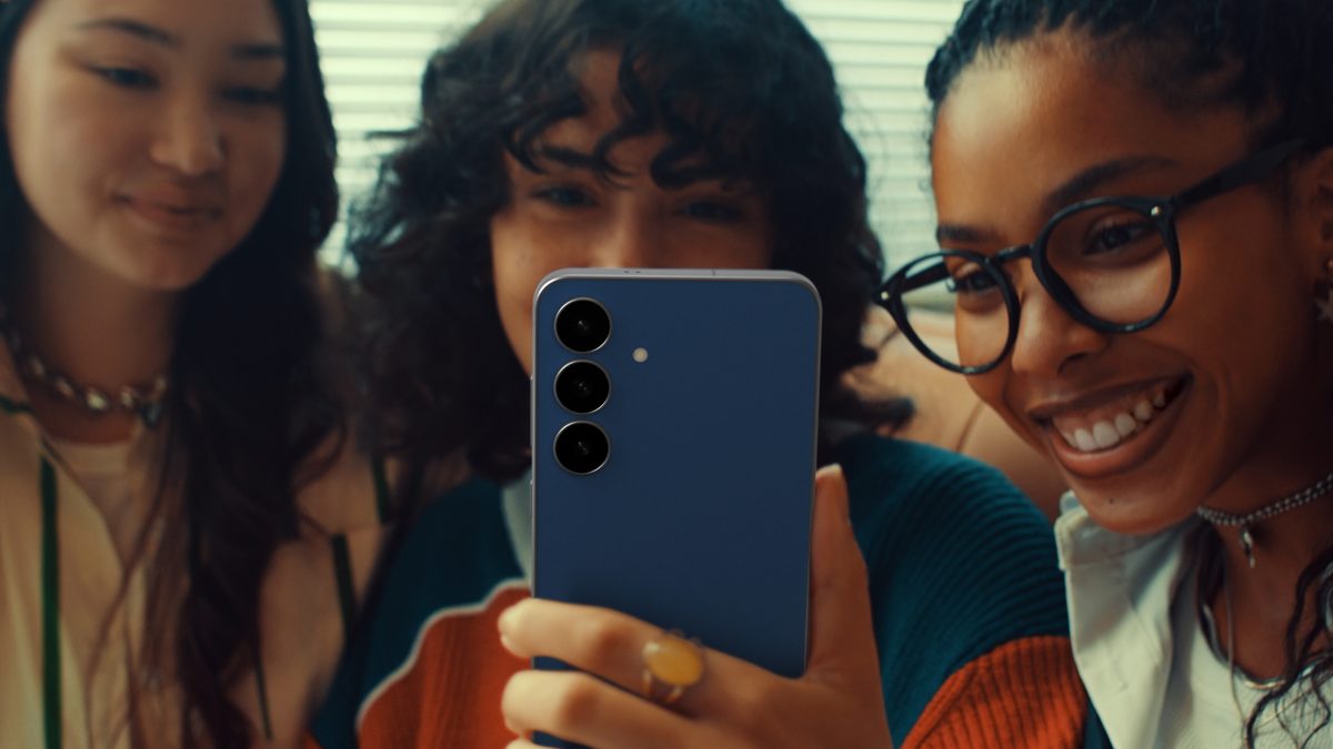 Três jovens olham para um Galaxy S25 FE azul, visto de costas, em imagem de divulgação da Samsung