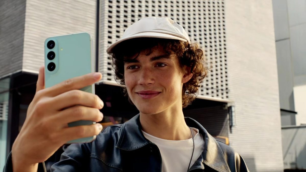 Jovem segura o Galaxy S26 FE verde-pistache, visto de costas, com as três câmeras à mostra