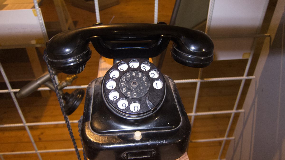 Telefone preto de disco, com o fone no gancho, apoiado sobre ripas de madeira