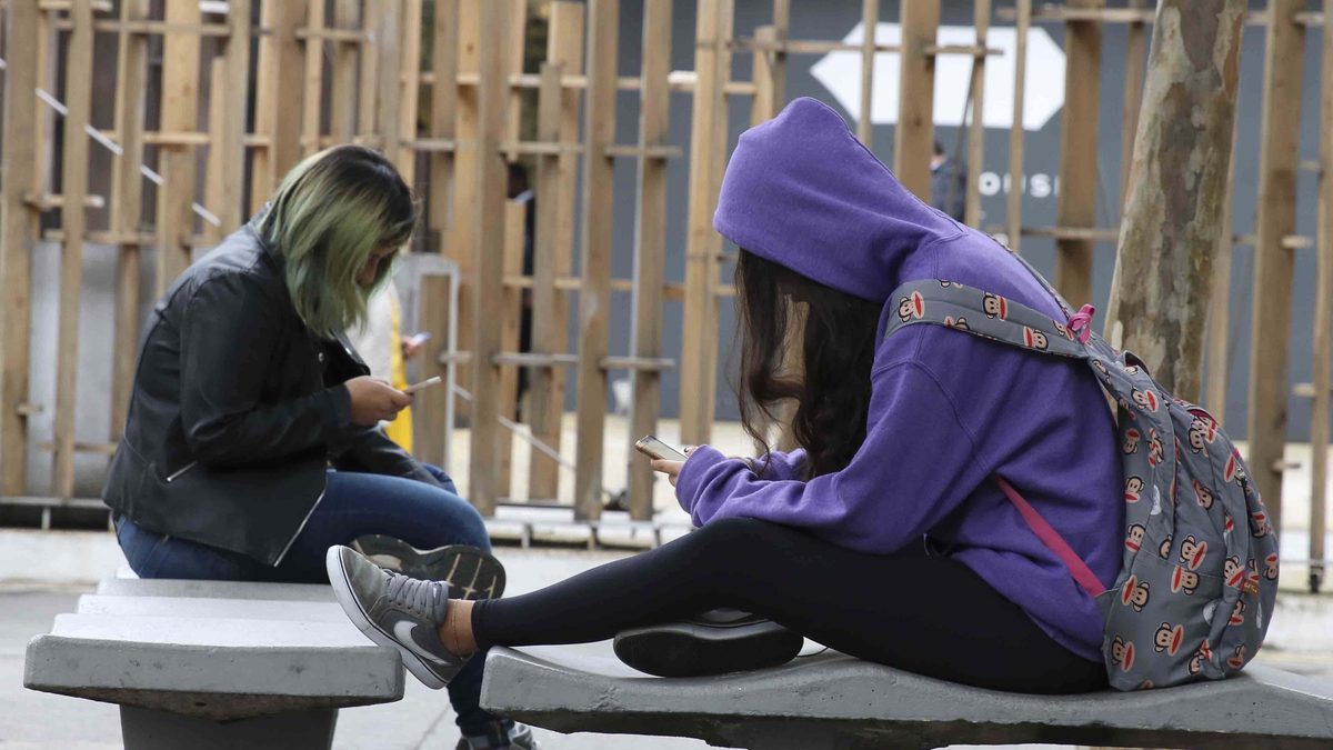 Duas pessoas sentadas usam celulares