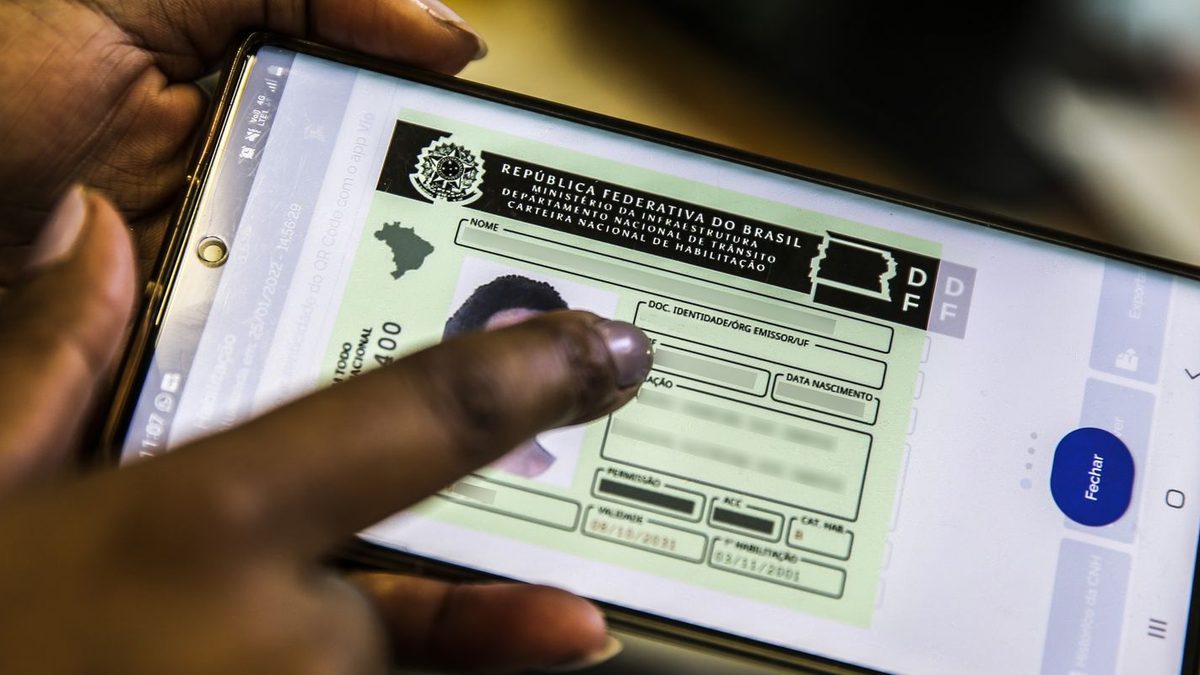 Mão aponta para a CNH digital aberta na tela de um celular, com os dados pessoais borrados, em foto de arquivo da Agência Brasil