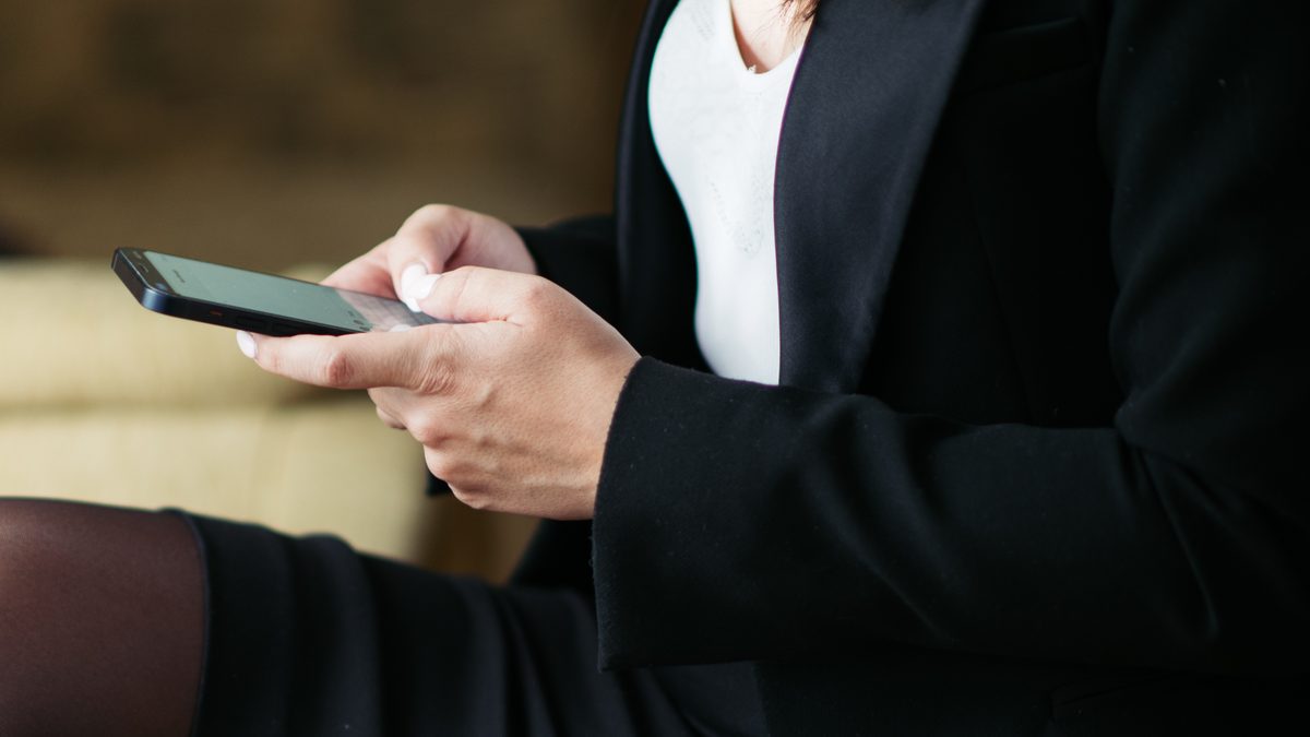 Mãos de uma pessoa de terno escuro digitando uma mensagem no celular