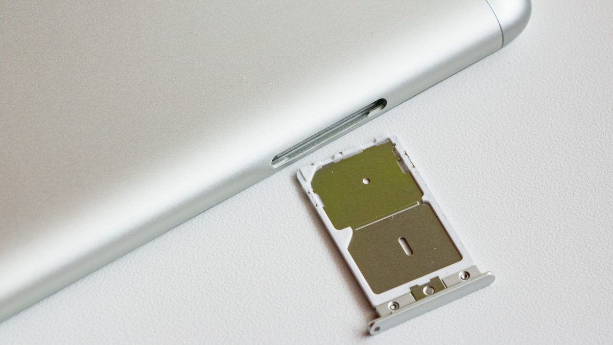 Bandeja para dois chips retirada da lateral de um celular prateado, apoiada sobre uma mesa branca