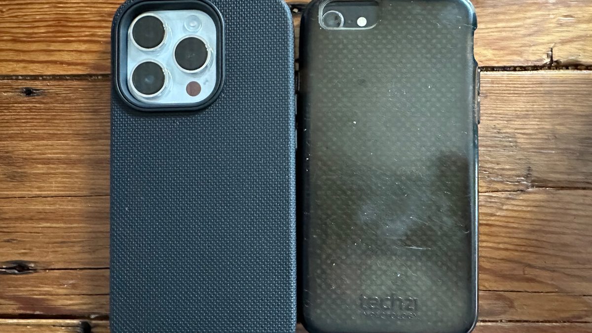 Dois iPhones de gerações diferentes lado a lado, com capinhas escuras, sobre uma mesa de madeira