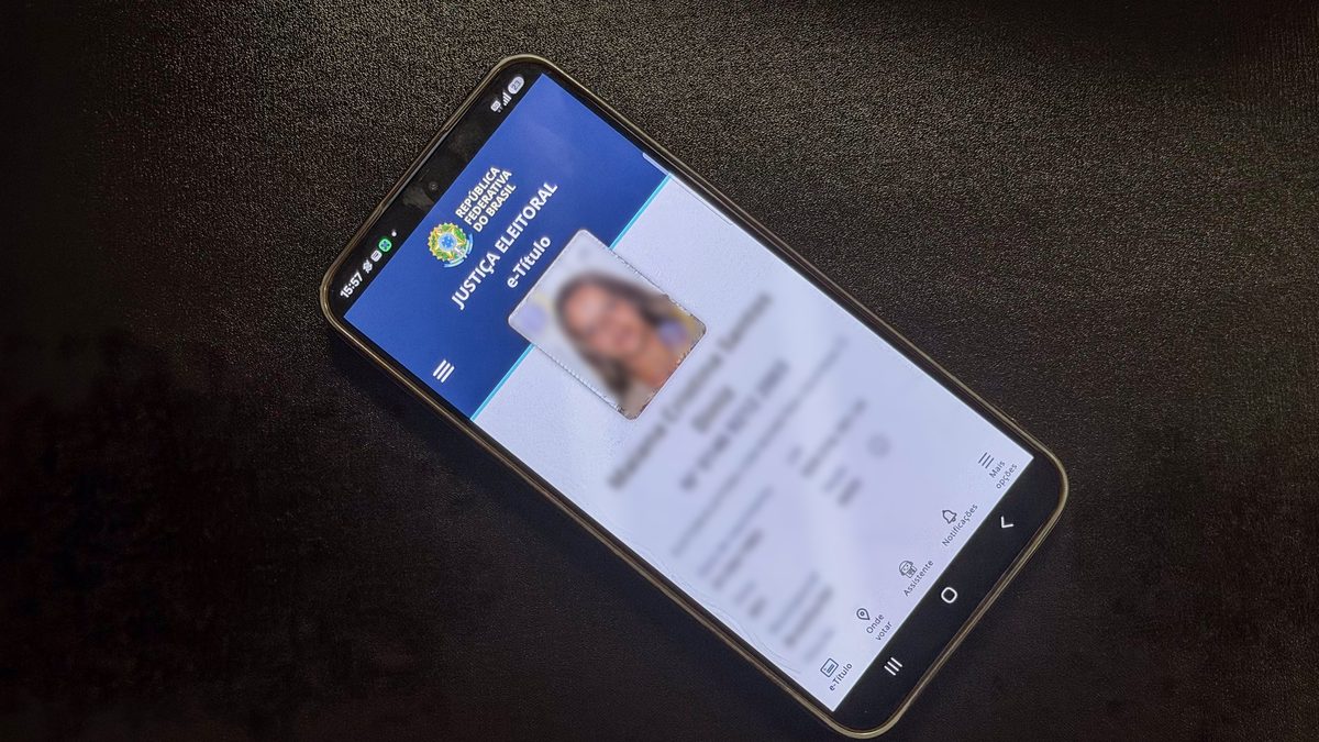 Celular sobre uma mesa escura exibe a tela inicial do aplicativo e-Título da Justiça Eleitoral, com foto e dados do eleitor desfocados