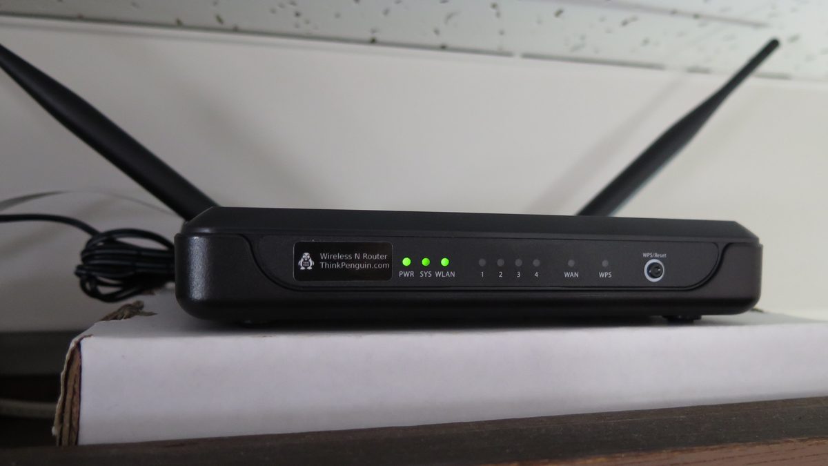 Roteador Wi-Fi preto com duas antenas erguidas e luzes verdes acesas, apoiado sobre uma caixa branca