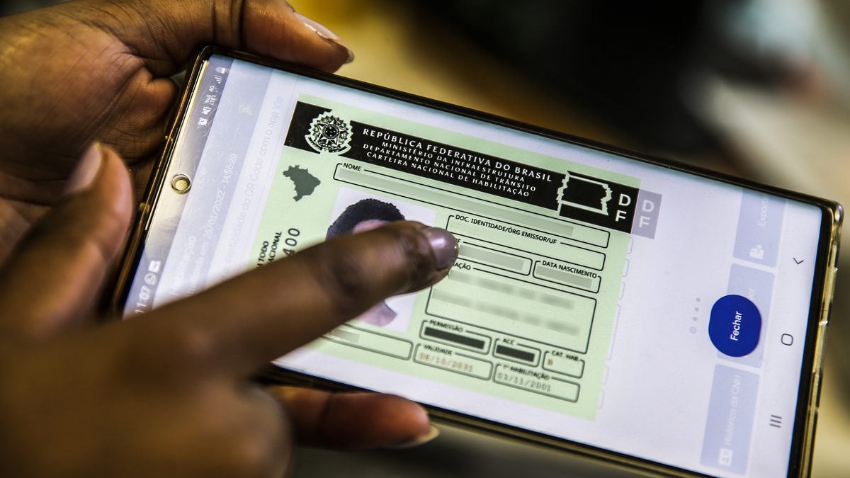 Mão segura celular com a CNH digital aberta no app federal de trânsito, com os dados pessoais borrados