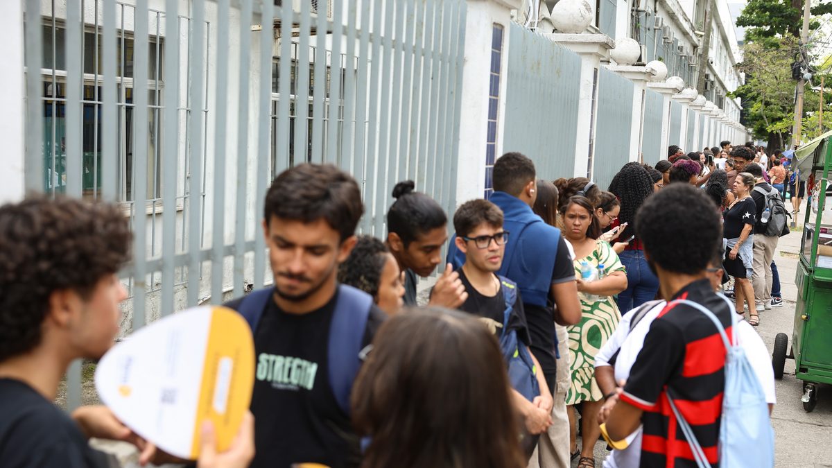 Estudantes em fila na calçada, junto à grade do Cefet Maracanã, no Rio de Janeiro, esperando a abertura dos portões no segundo dia do Enem 2025