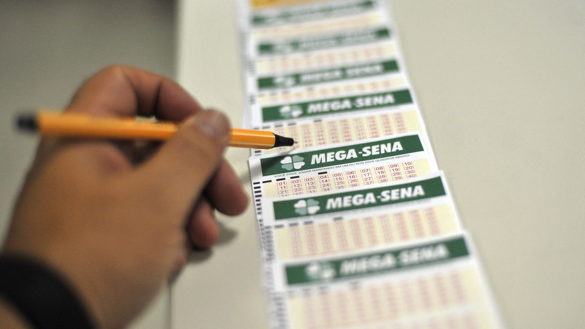 Mão com caneta sobre volantes da Mega-Sena em uma lotérica