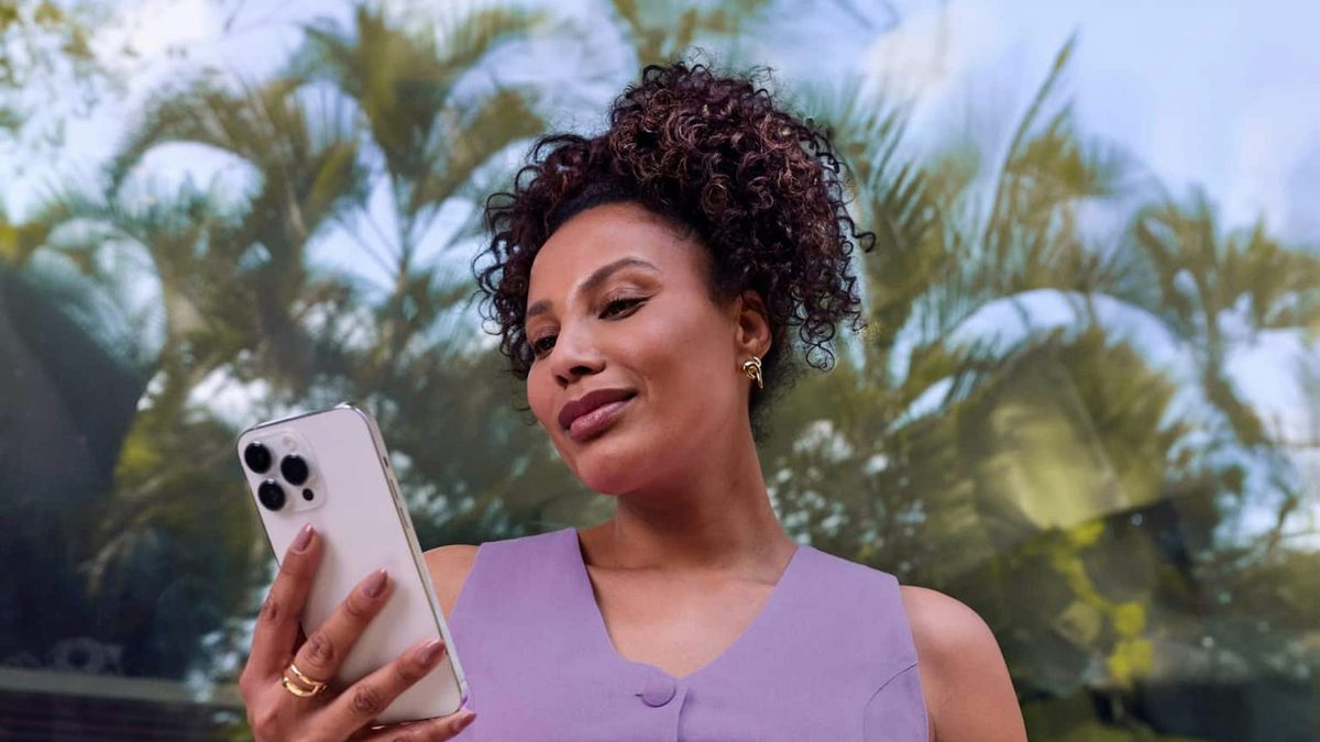 Mulher de colete lilás olha para um celular que segura com a mão direita, ao ar livre, em imagem de divulgação do Nubank