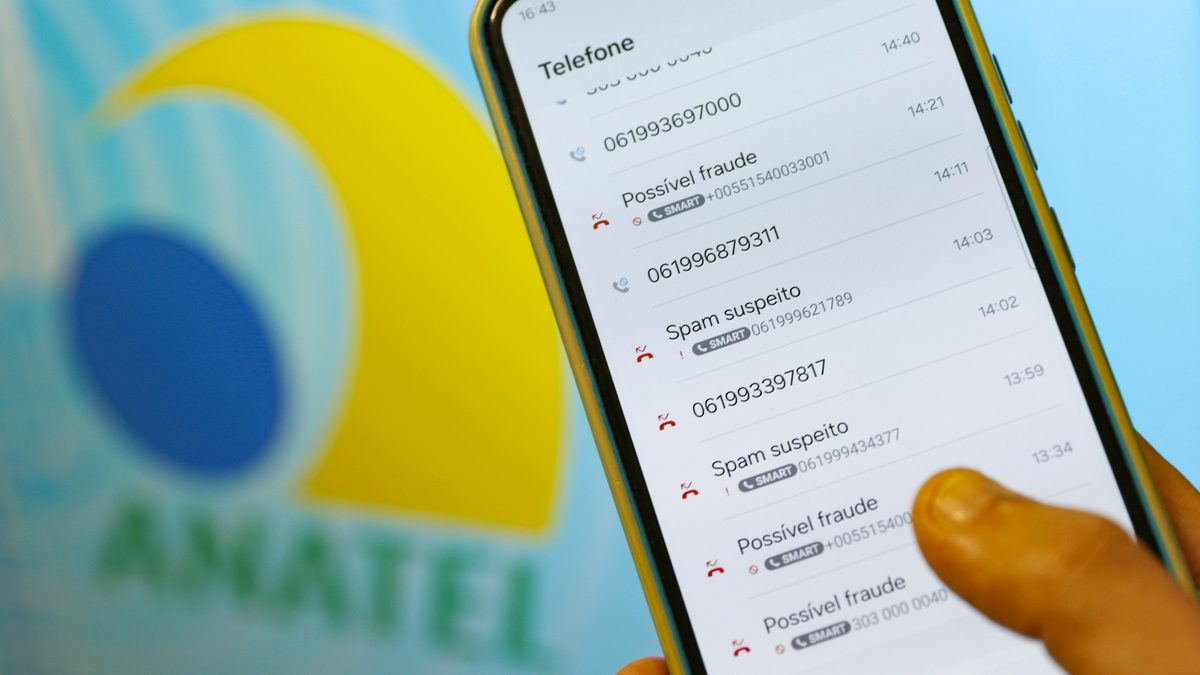 Mão segura celular com a lista de chamadas marcadas como spam suspeito e possível fraude, com a marca da Anatel ao fundo, em Brasília, em janeiro de 2025