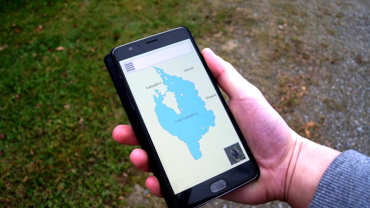 Mão segurando um celular com um mapa aberto na tela, ao ar livre, sobre um caminho de terra e grama