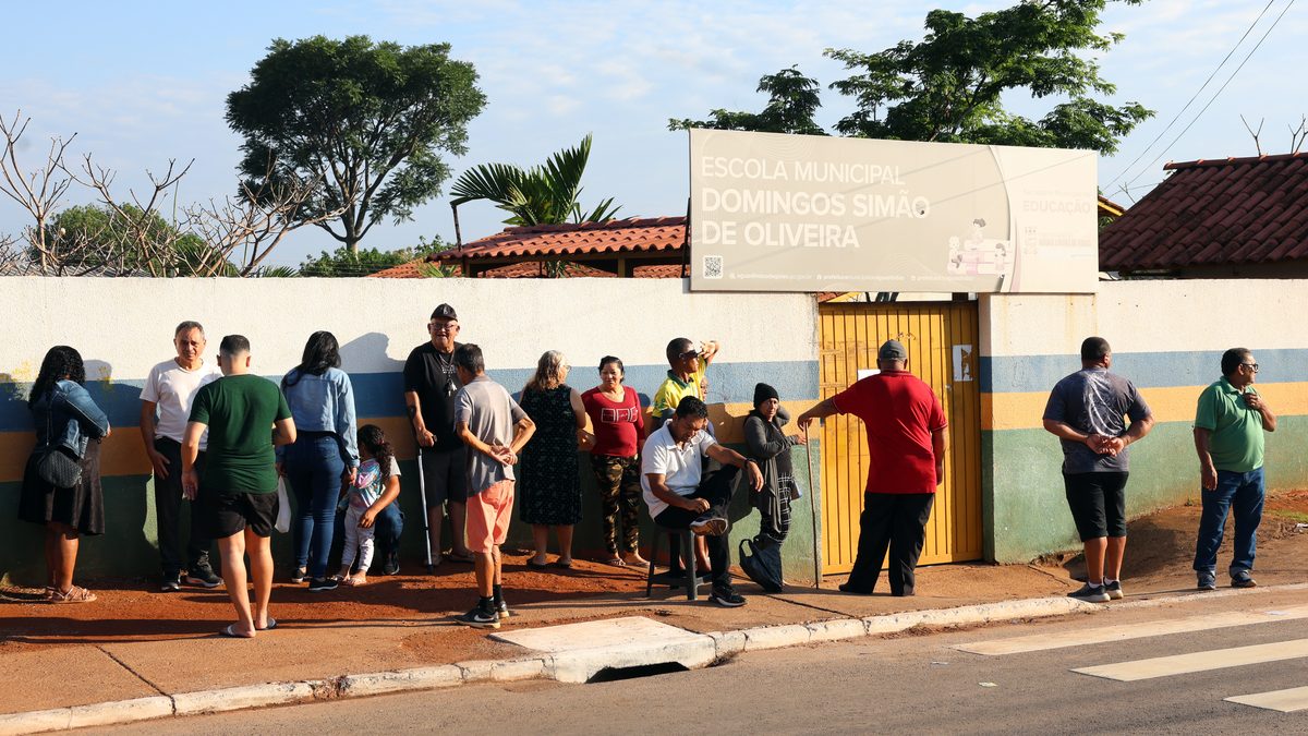 Eleitores aguardam em calçada diante da Escola Municipal Domingos Simão de Oliveira, em Águas Lindas de Goiás, na votação das Eleições 2026