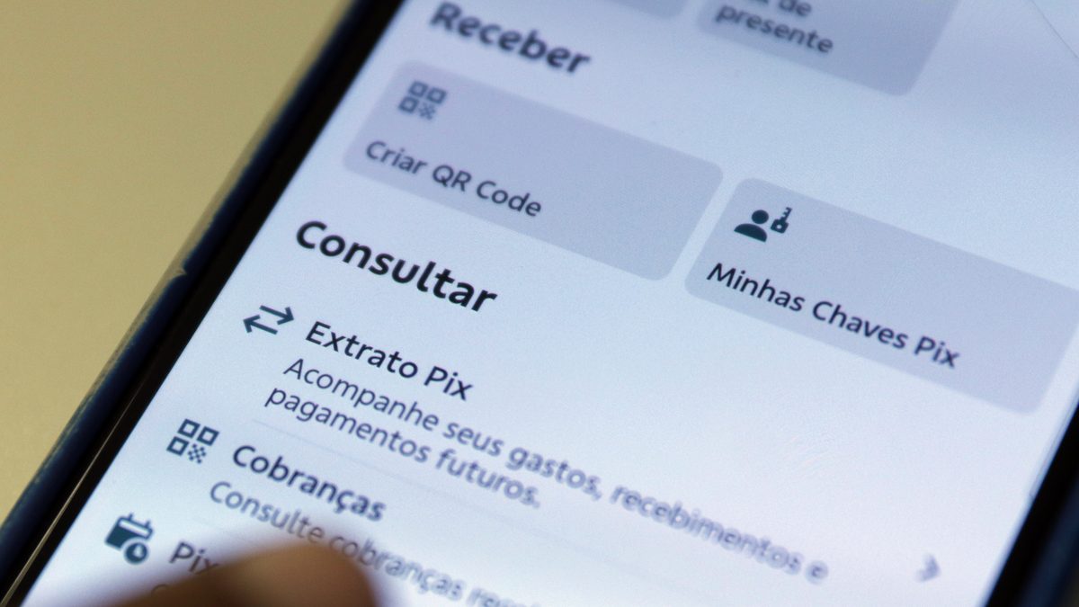 Dedo tocando a tela de um celular aberta na Central Pix de um aplicativo de banco, com as seções Receber e Consultar, Extrato Pix e Minhas Chaves Pix