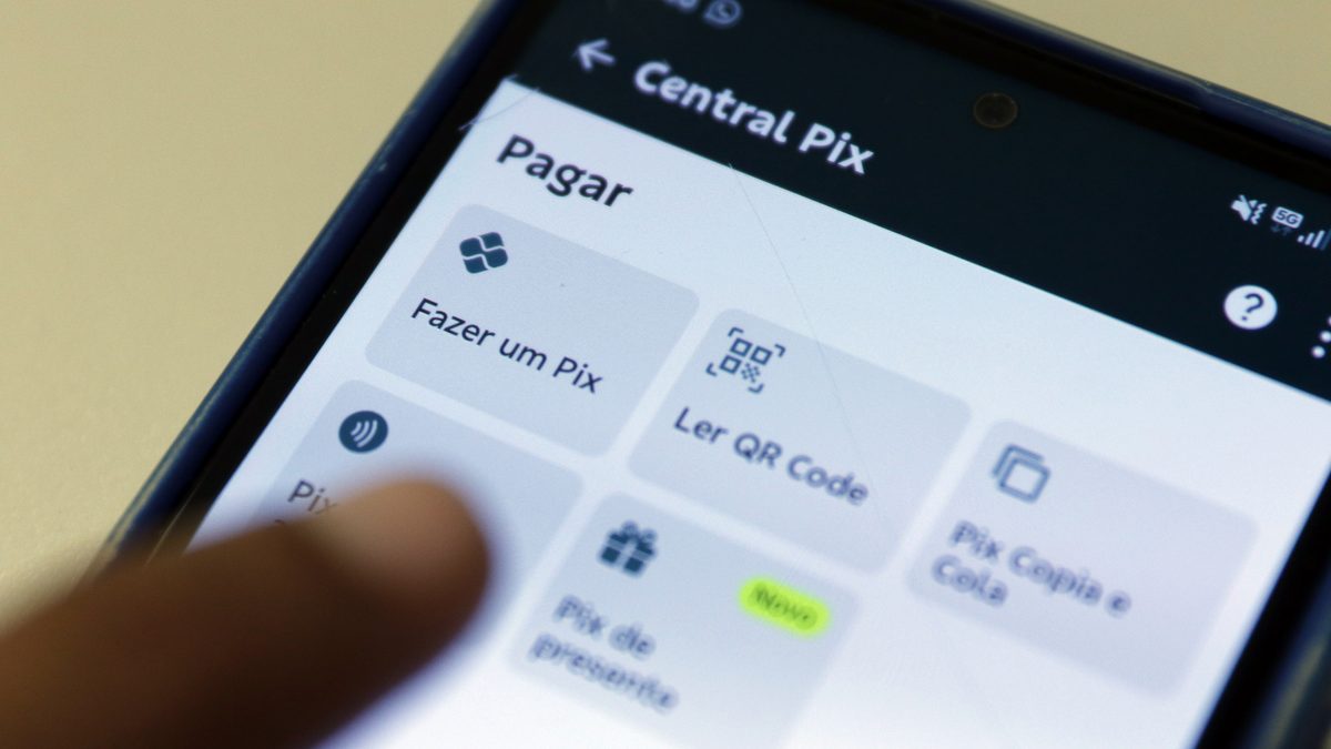Dedo tocando a tela de um celular aberta na Central Pix de um aplicativo de banco, com as opções Fazer um Pix e Ler QR Code