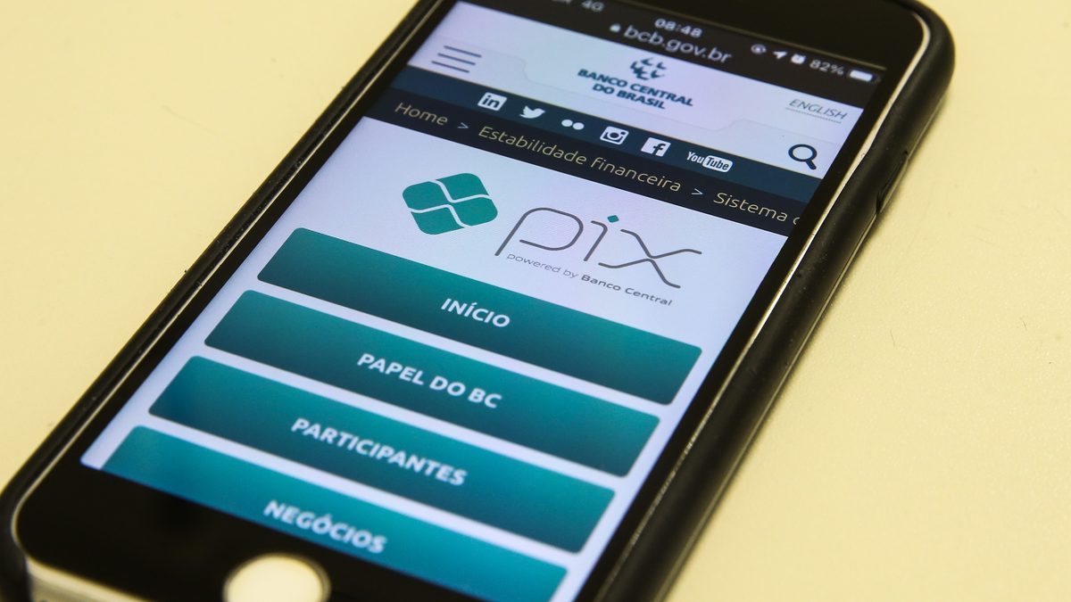 Celular sobre a mesa com a página do Pix no site do Banco Central aberta, com os botões Início, Papel do BC e Participantes