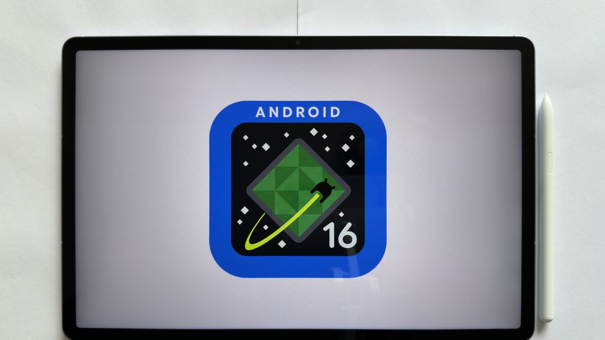 Tablet sobre uma mesa branca exibindo o emblema do Android 16 na tela, com uma caneta ao lado