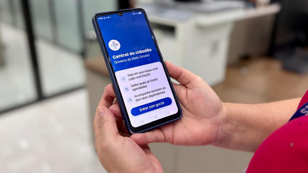 Mãos seguram um celular com a tela inicial do aplicativo do governo de Mato Grosso, com o botão Entrar com gov.br, em foto de divulgação da SES-MT
