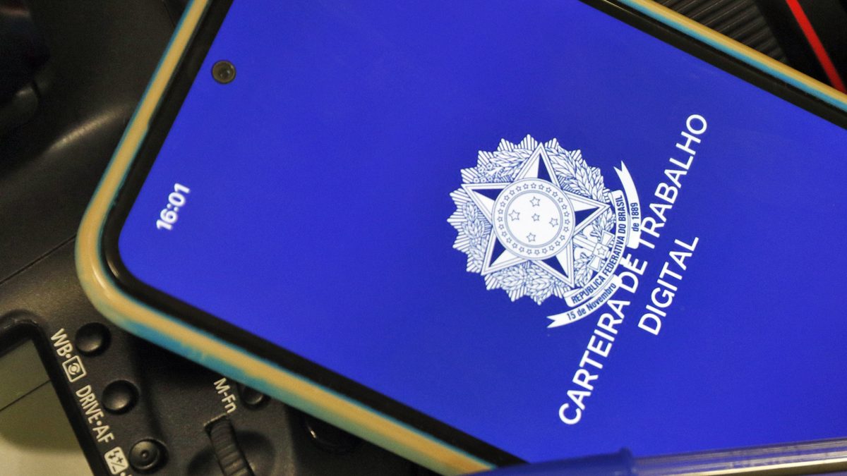 Tela de abertura do aplicativo Carteira de Trabalho Digital, com o brasão da República, em um celular apoiado sobre uma câmera e um teclado