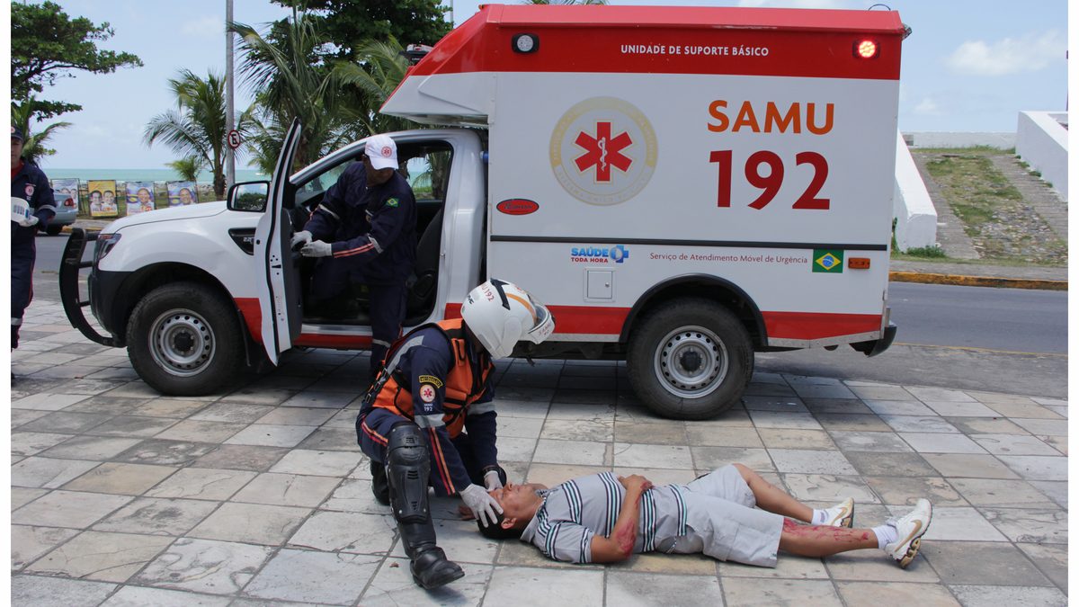 Socorrista do SAMU 192 atende um homem deitado na calçada, ao lado da ambulância, em Olinda