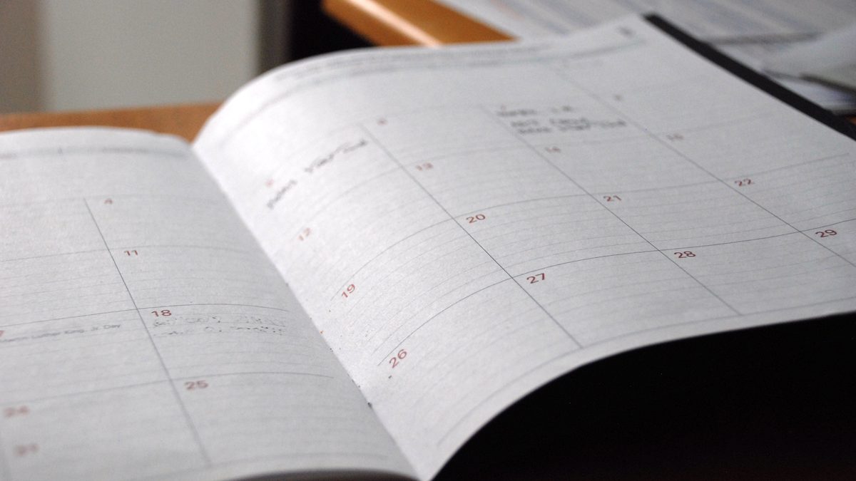 Agenda de papel aberta na página do mês, com os dias numerados em quadros, sobre uma mesa de madeira