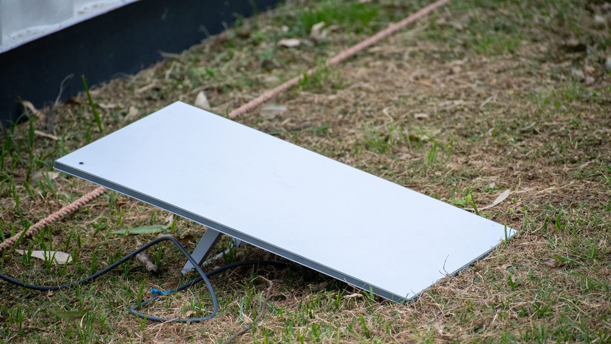 Antena de internet por satélite da Starlink apoiada em um suporte sobre um gramado, com o cabo no chão