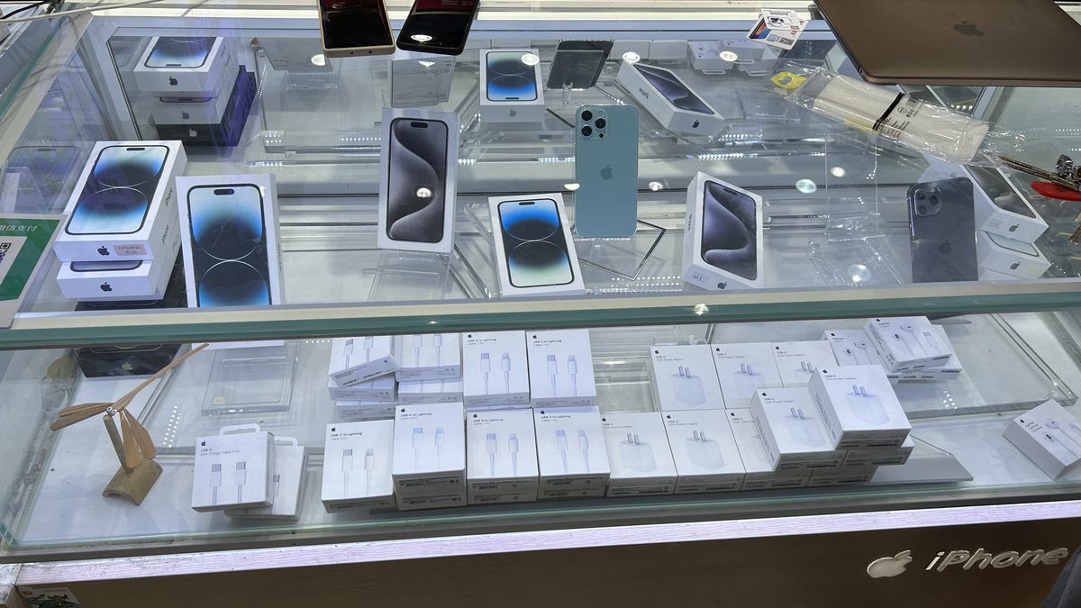 Vitrine de vidro de uma loja de celulares com vários iPhones expostos em cima e caixas de acessórios brancas embaixo