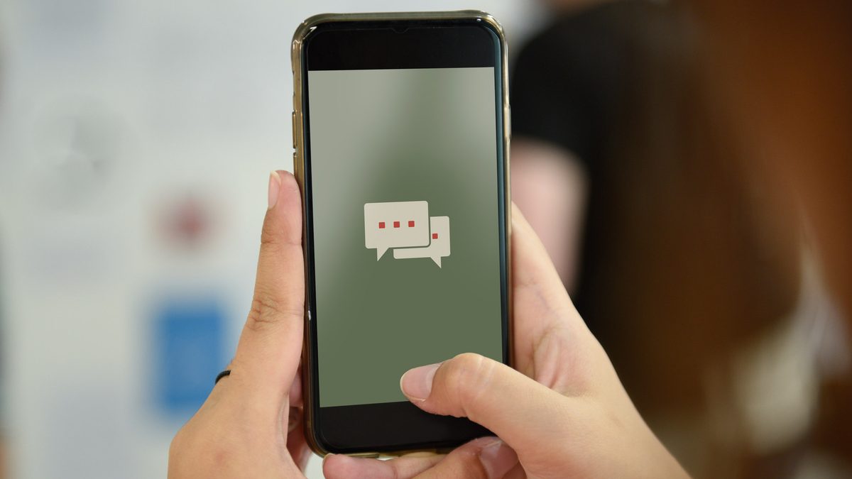 Duas mãos segurando um celular com ícone de balões de conversa na tela