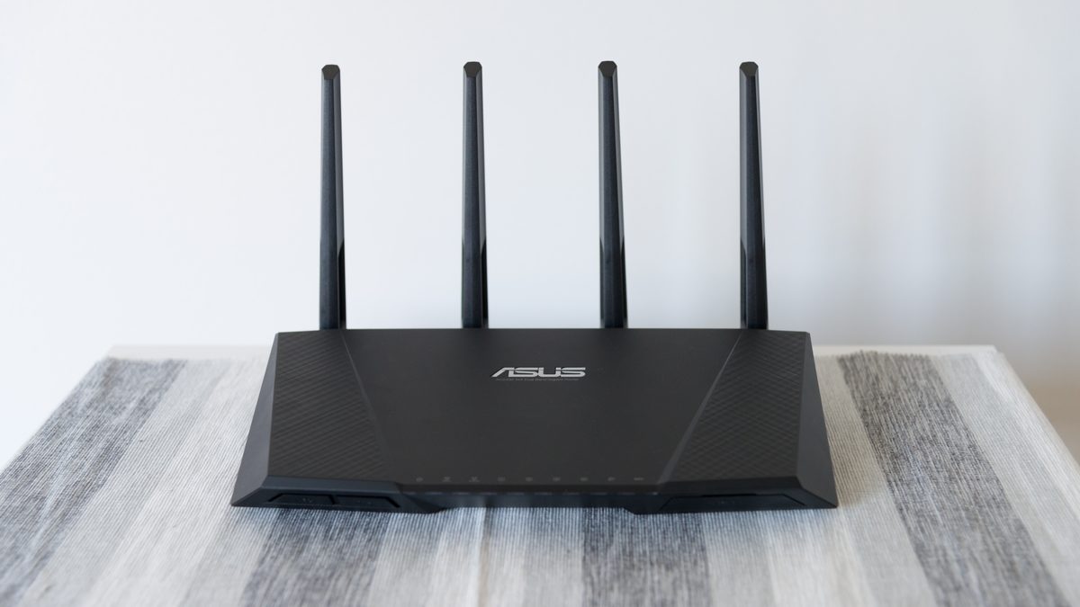Roteador Wi-Fi preto com quatro antenas para cima sobre uma mesa com toalha listrada cinza