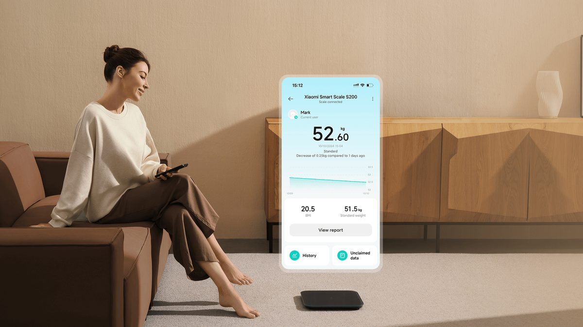 Mulher sentada no sofá olha o celular, com a tela do app Xiaomi Home mostrando o peso medido pela balança Smart Scale S200, que aparece no chão